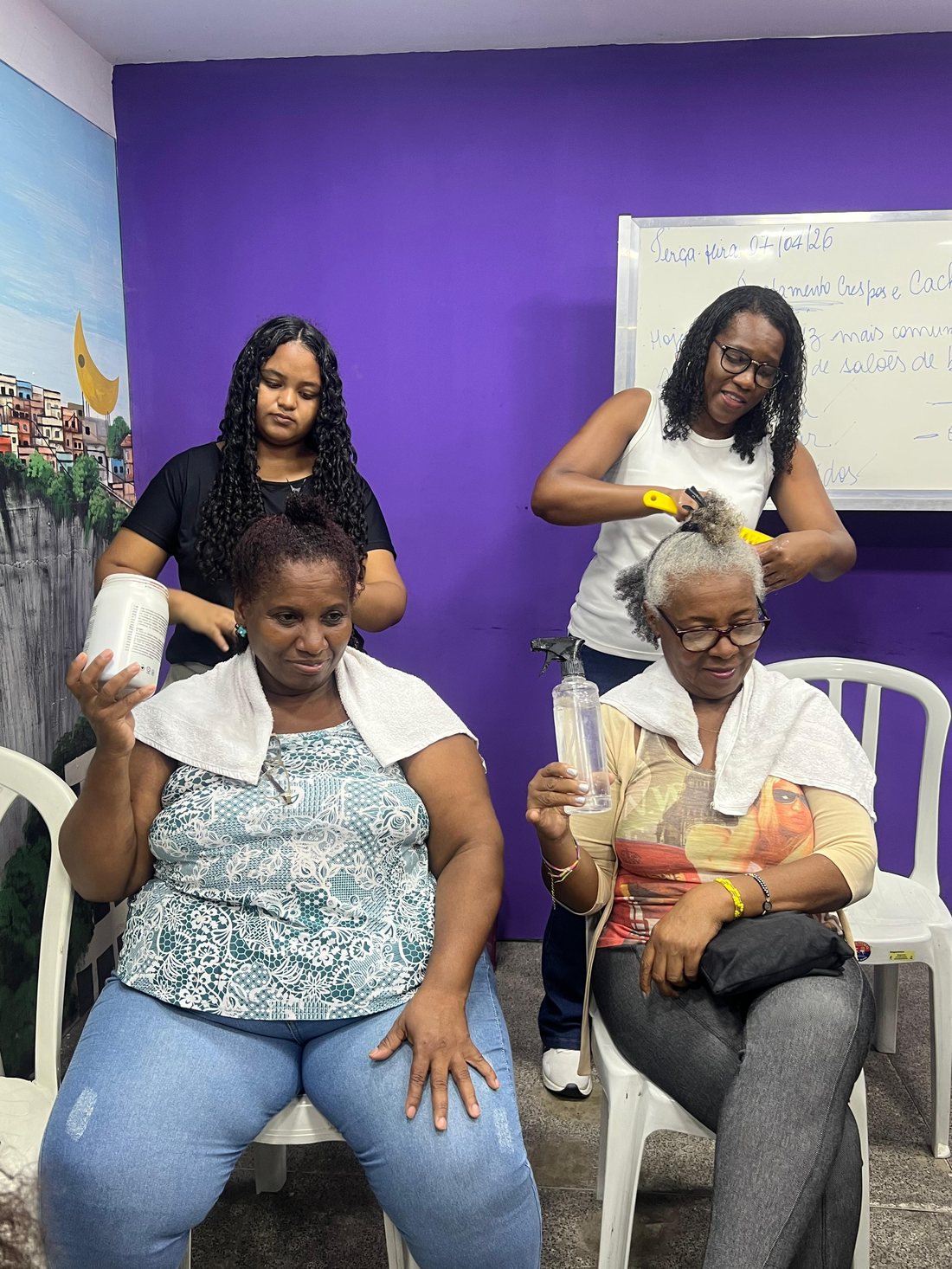 Duas profissionais do Instituto Ayó cuidam do cabelo de duas moradoras sentadas durante a oficina