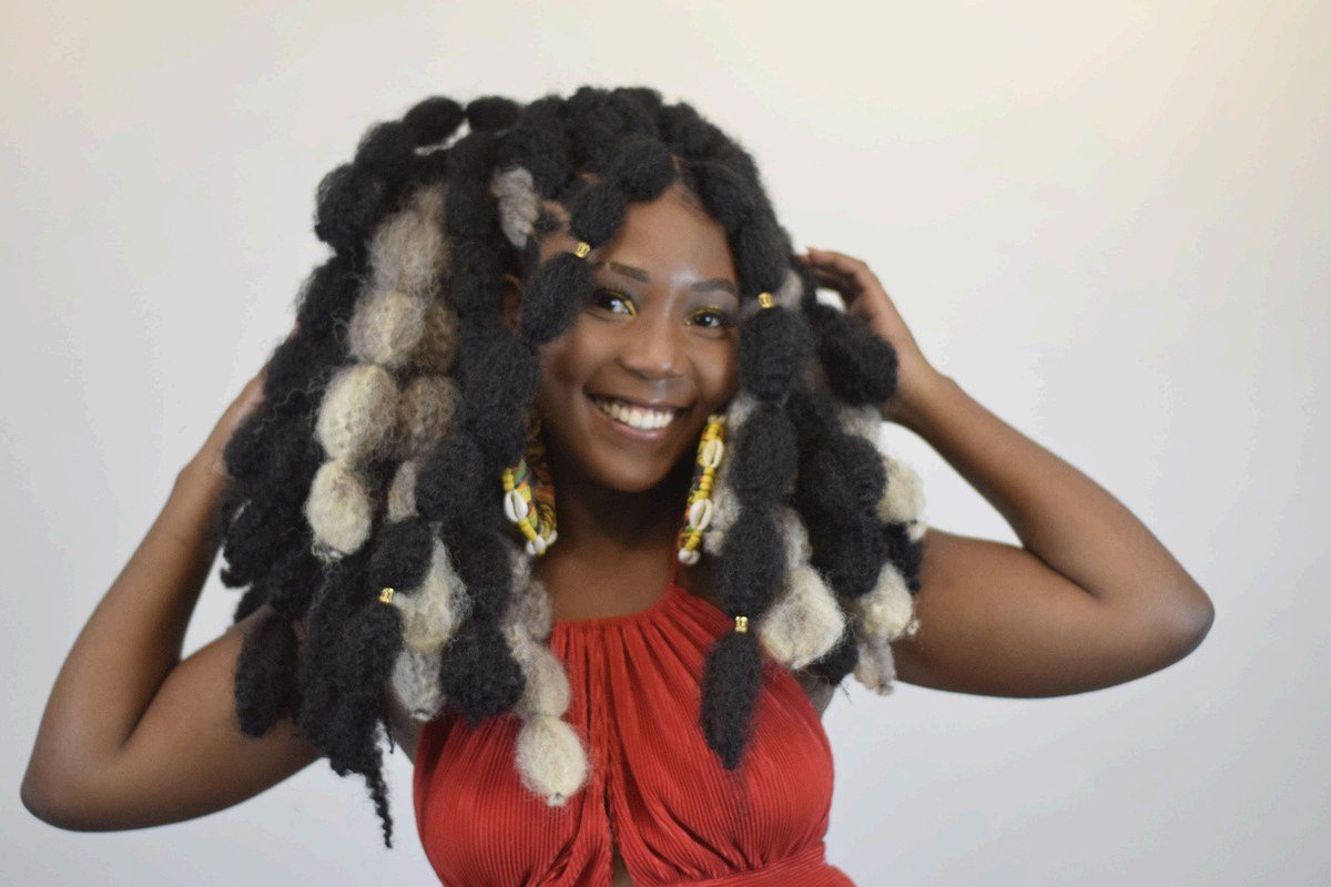 Mulher negra sorri exibindo o penteado de tranças finalizado na oficina do Instituto Ayó