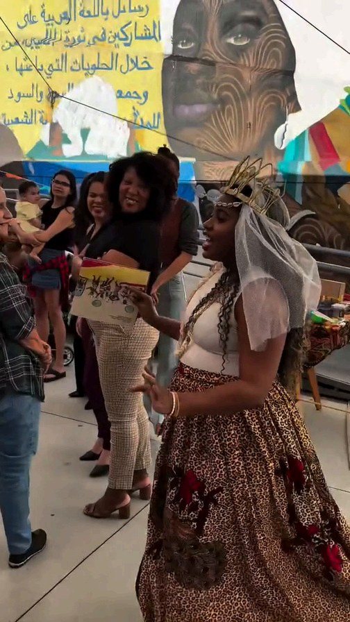 Apresentação cultural durante o Arraiá das Pretas, com participante em traje de festa junina diante de um mural colorido